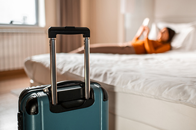 traveler reading on hotel bed with blue luggage at front