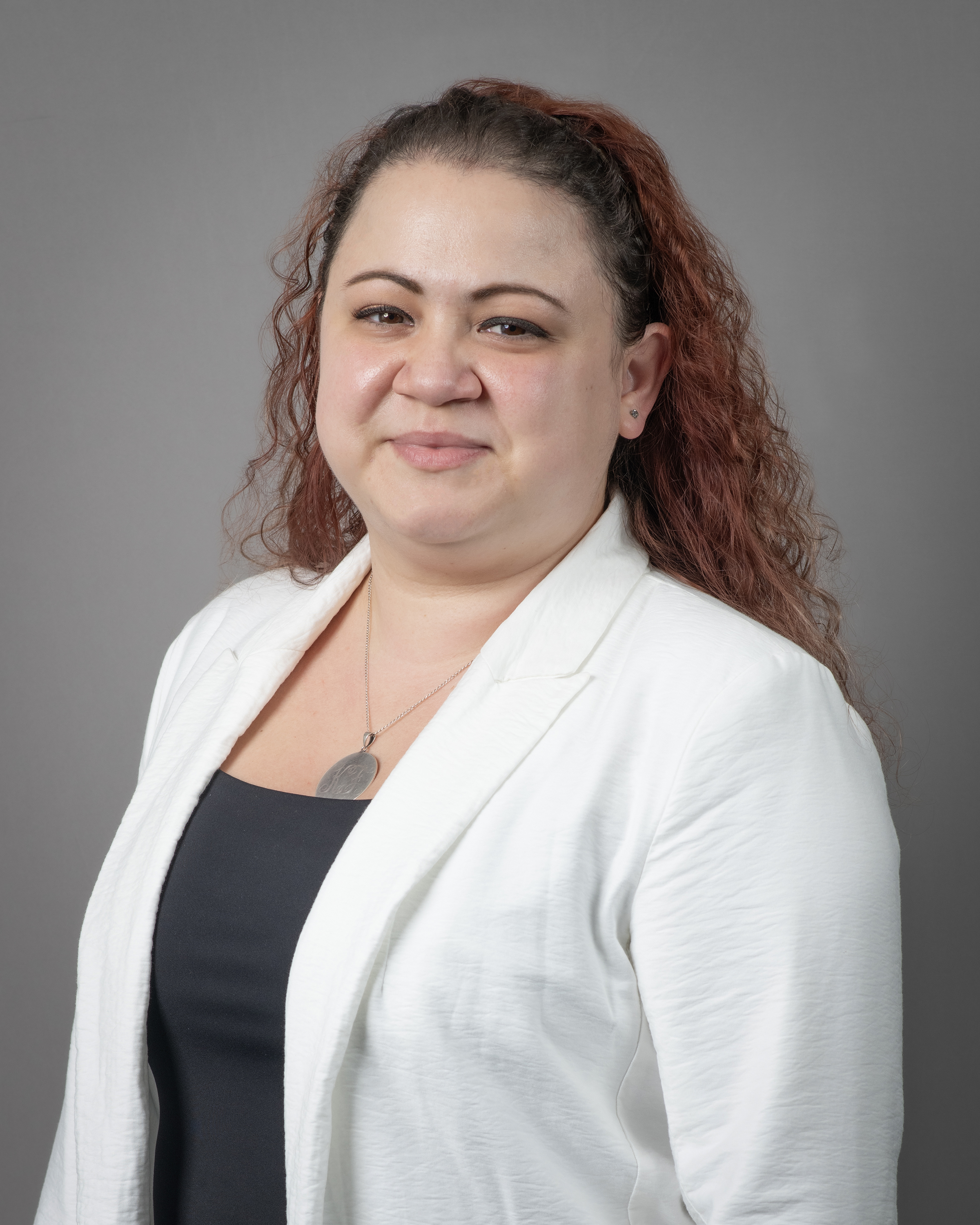Karina Falcone smiling for a headshot, wearing a white blazer and black blouse