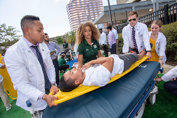Interprofessional Health Education practice exercise photo with students helping a standardized patient on a gurney in downtown Tampa