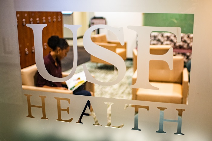 USF Health logo on glass with student reading behind it