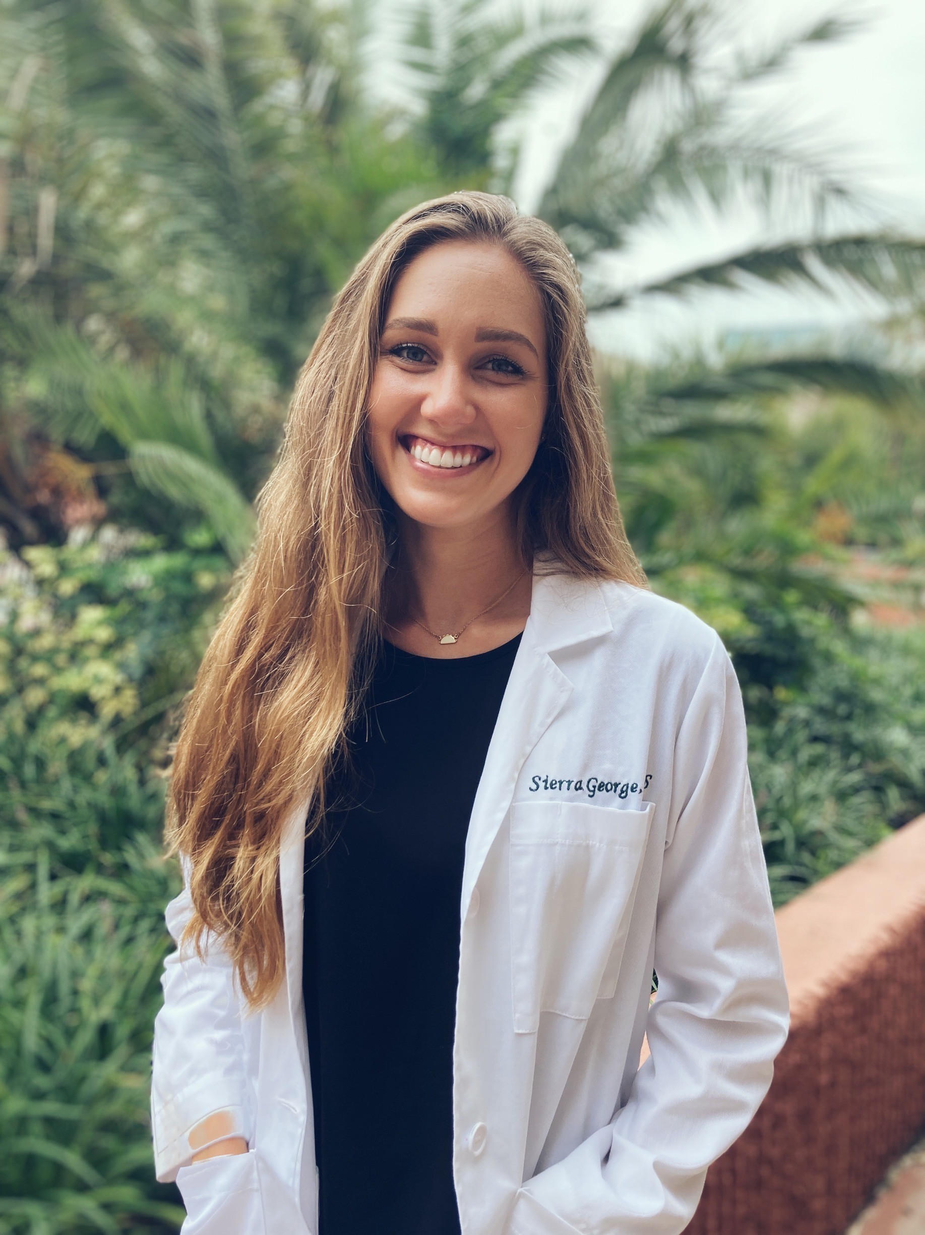 Photo of Sierra George in white coat outside in front of palm trees