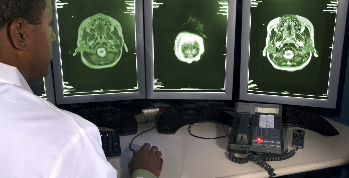 Doctor in front of 3 monitors performing a CAT Scan