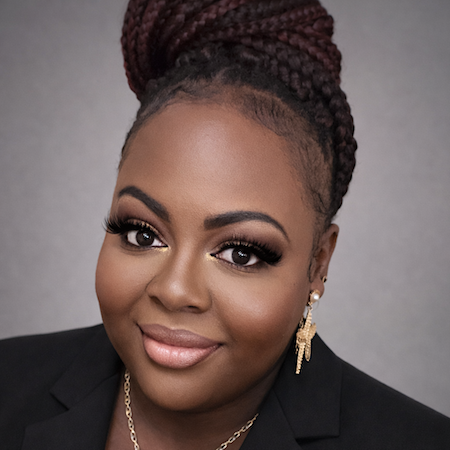 A woman smiles dressed in a black suit jacket and wearing dangly gold earrings