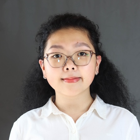 A woman with long dark hair and glasses smiles in a white collared shirt