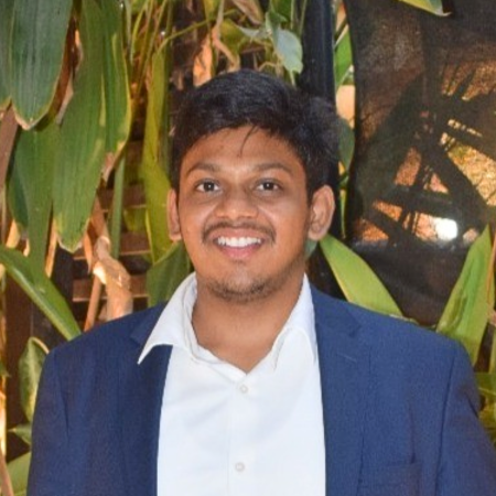 A male student with short brown hair smiles in a white shirt and blue suit jacket