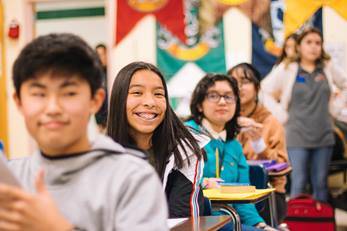 Students in a classroom setting, with a smiling young girl in focus.