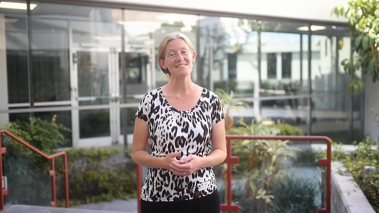 Dr. Jill Roberts smiling outdoors in a black and white top, standing in front of palm trees and greenery.