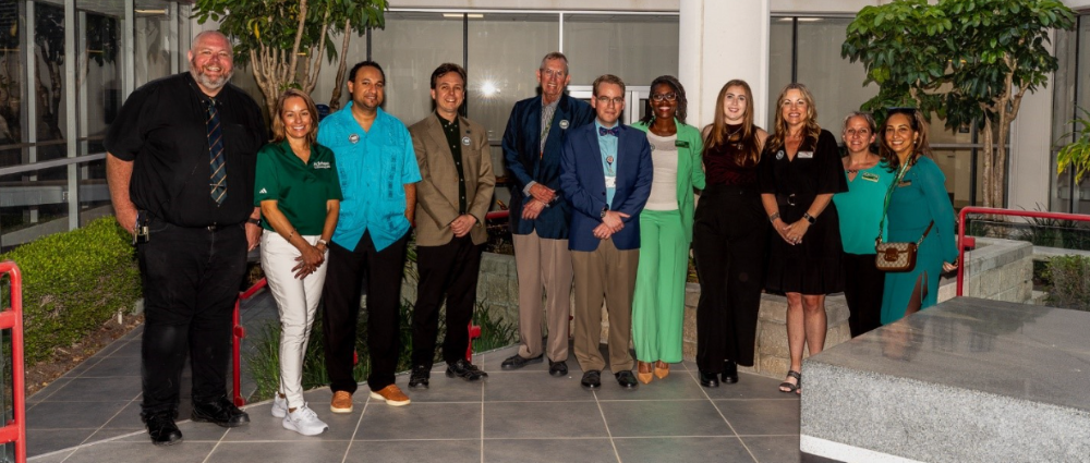 A group of COPH alumni posing together and smiling at the COPH building