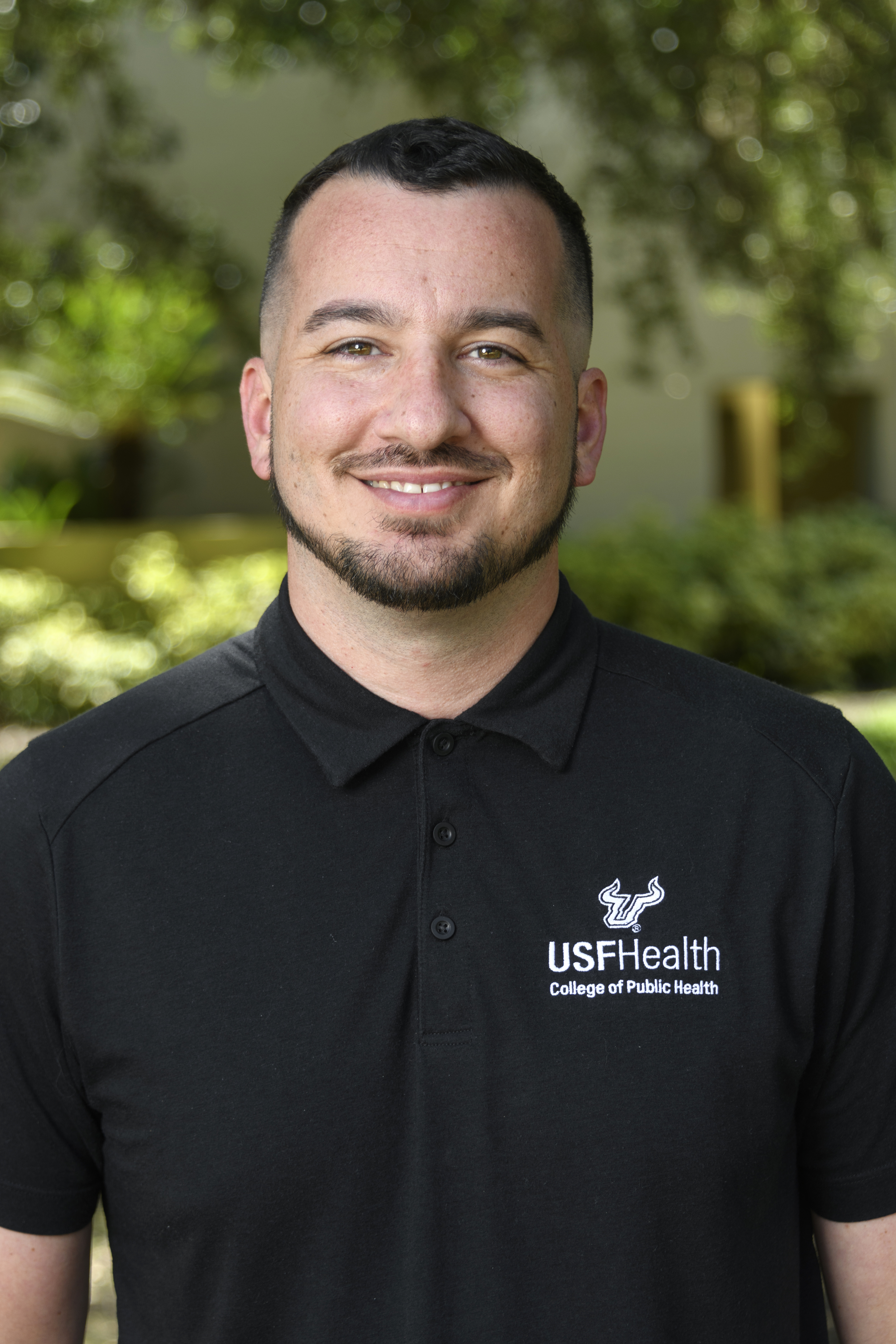 A headshot of Dr. Anthony Iannelli smiling in front of an outdoor backdrop. He is wearing a black shirt with the USF Health logo