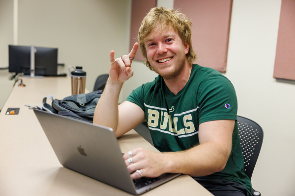 A student on his computer holding up the "Go Bulls!" hand symbol