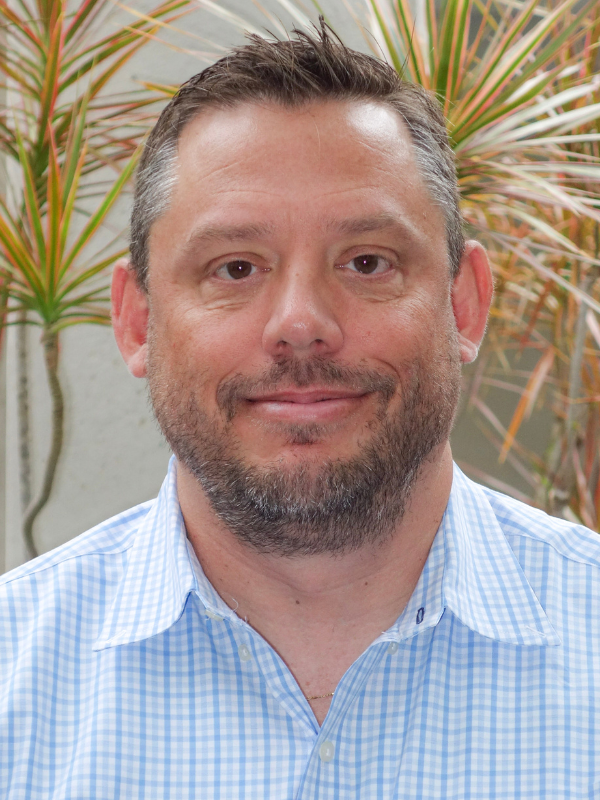 A headshot of Jay Evans smiling in an outdoor setting