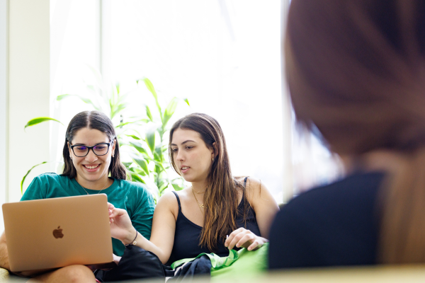 Two women sit on a couch, focused on a laptop, engaged in conversation and sharing ideas.