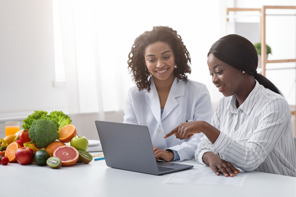 Two public health professionals having a discussion while looking at a laptop next to a plate of fruits and vegetables