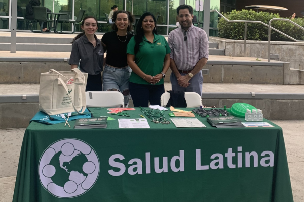Volunteers from Salud Latina participate in activities at a green table, fostering community health and support initiatives.
