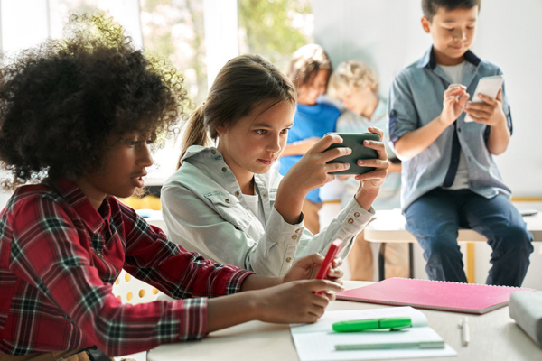 A group of children sitting at a table with their cell phones.