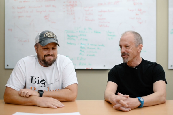 Hosts Marty Martin, and Art Woods sit at a wooden table in discussion.