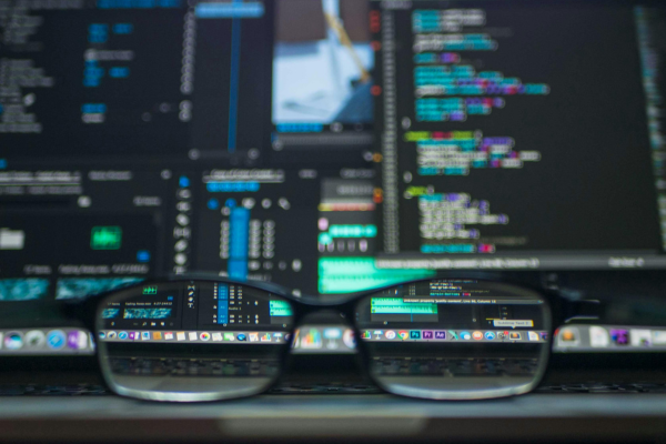 A pair of glasses in the foreground of multiple computer screens showcasing epidemiological research