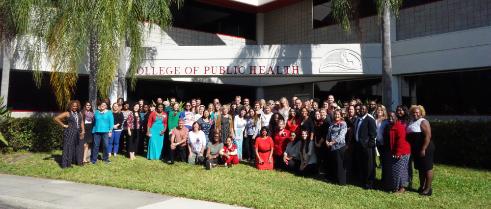 A large group of faculty and staff in front of the USF College of Public Health Samuel P. Bell, III building.