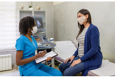 A patient wearing a mask speaking to a nurse wearing a mask