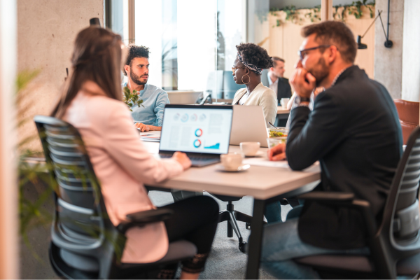 A group of people sitting at a table in an office working on their laptops