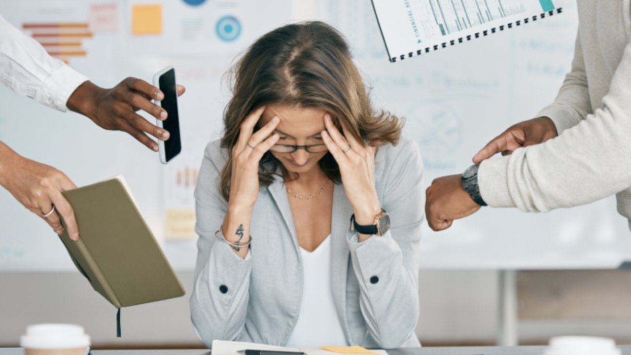 A person sitting at a desk with their hands on their head