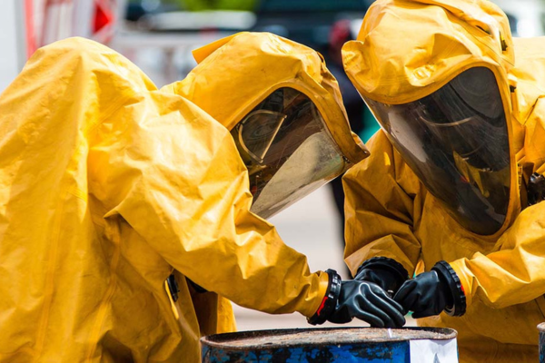 Two people in yellow hazmat suits working on a barrel