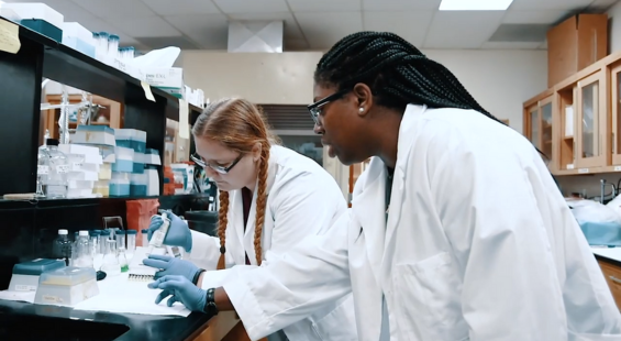Two students in lab coats conducting research in a laboratory, surrounded by scientific equipment.