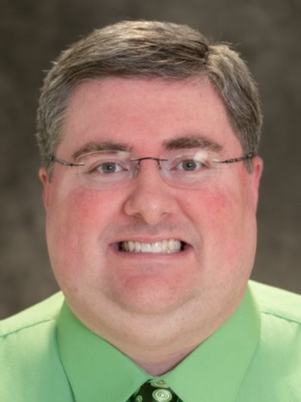 Headshot of Adam Clum smiling in front of a grey backdrop
