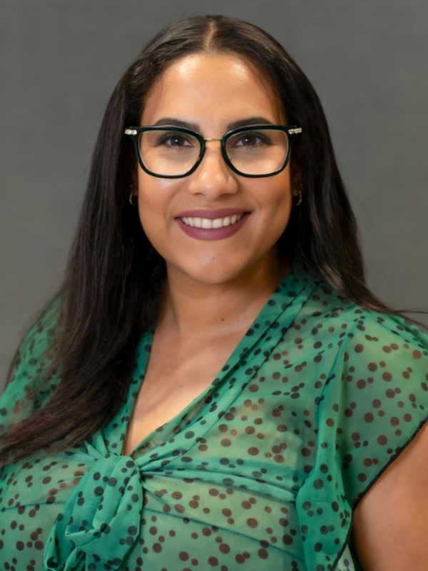 Headshot of Elissa Santos smiling in front of a grey backdrop