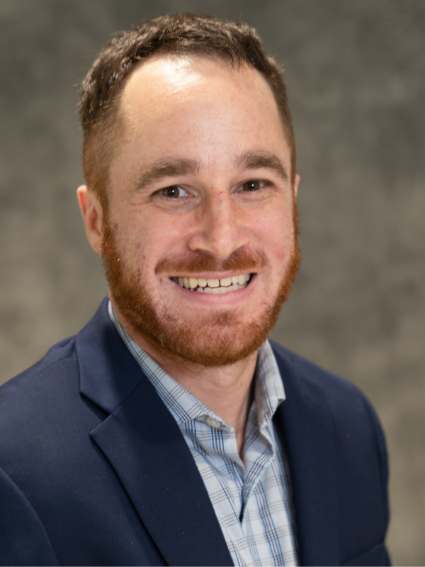 Headshot of Luke Newton smiling in front of a grey backdrop
