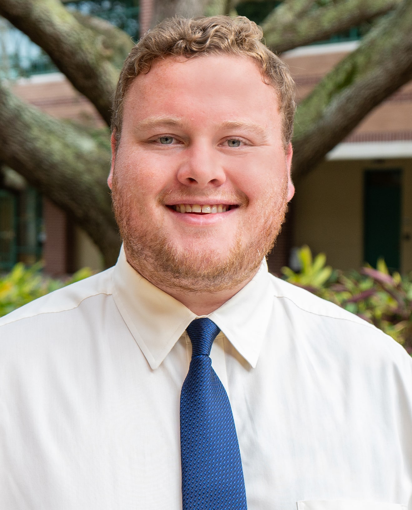 Daniel Surfass smiling wearing a white shirt and blue tie