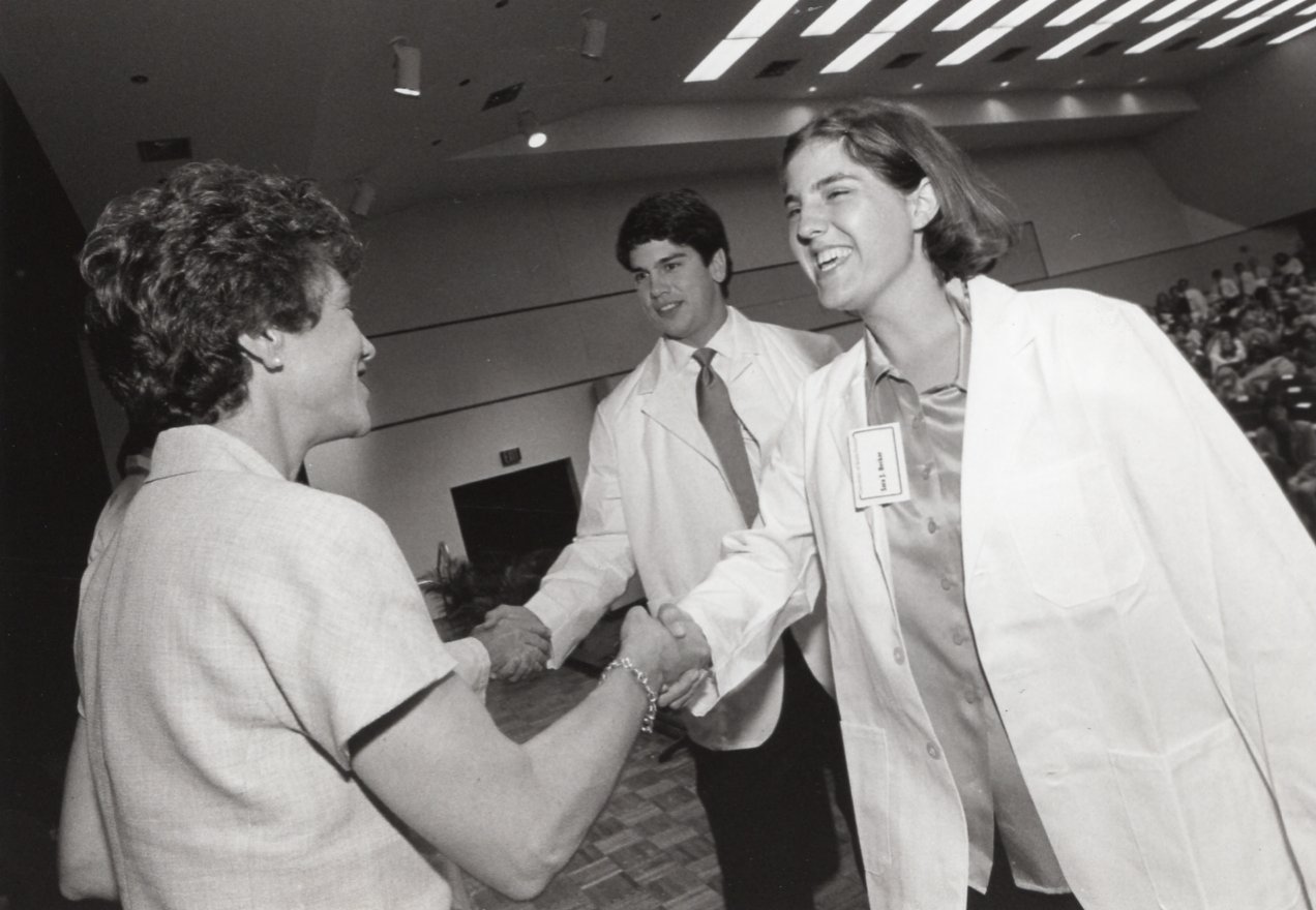 Black and White still of Dr. Genshaft shaking hands with two doctors at the white coat ceremony