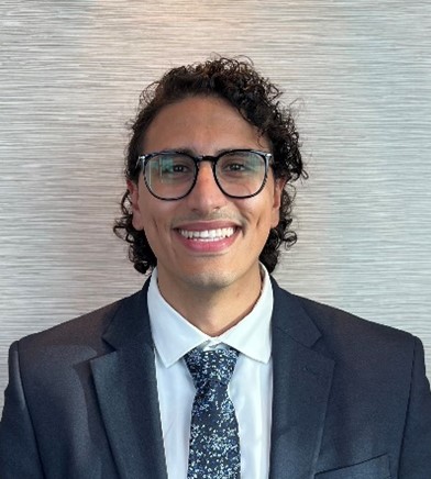 Antony smiling wearing a suit and tie with black framed glasses