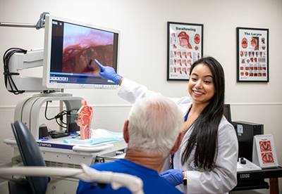 USF Health Voice Center physician smiles at patient while pointing to a computer display showing an image of his vocal chords