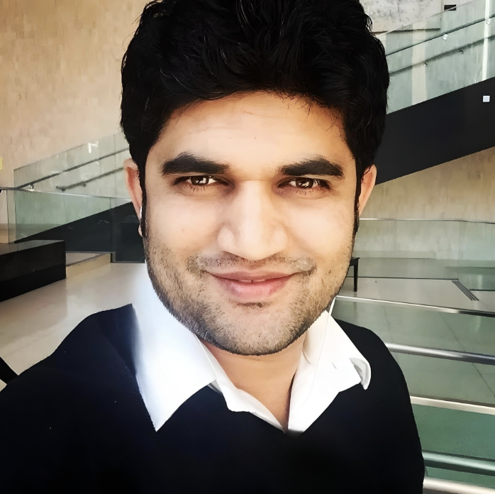 Ajit Magadum smiling wearing a white collard shirt and black sweater