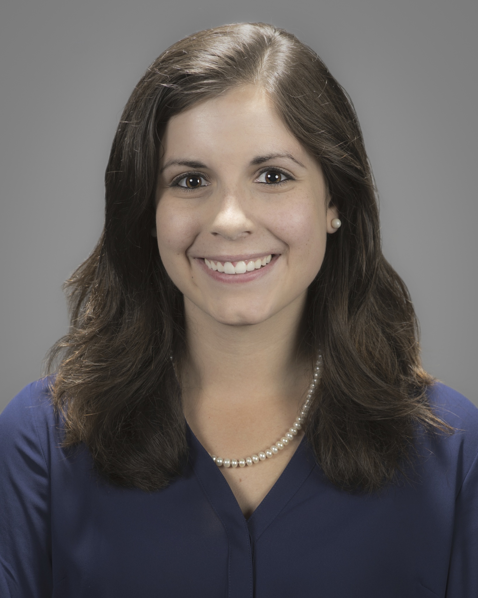 Jacqueline Koelker smiling wearing a navy blue blouse and white pearl necklace