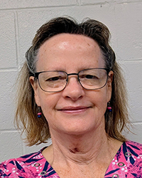 Laura Pendleton smiling earing a pink and black blouse with floral design