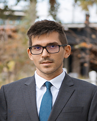 Michael McClain headshot wearing a dark grey suit with white shirt and blue tie