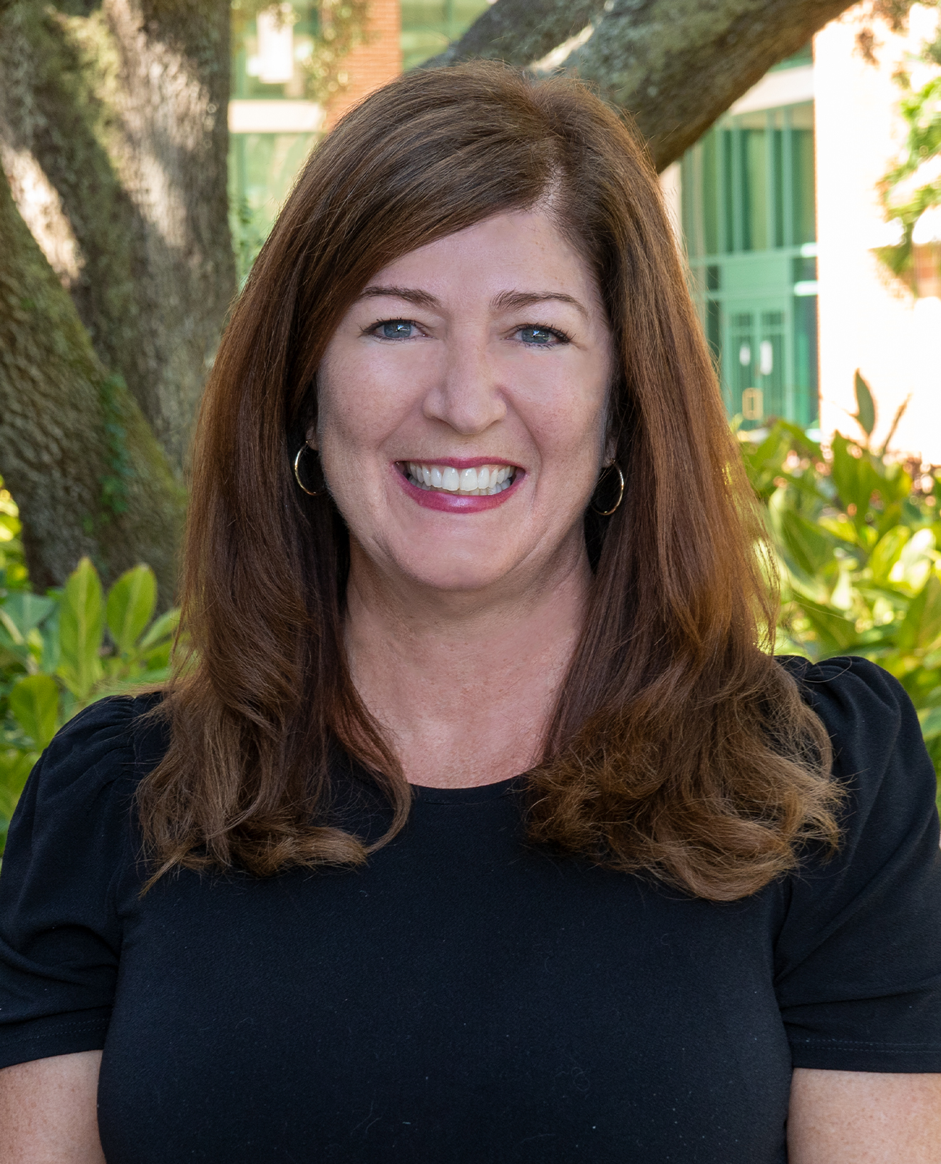 Stefanie Seropian smiling wearing a black blouse standing in front of tropical landscape
