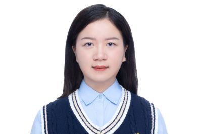 Xueling Ma smiling wearing a blue dress short with navy blue sweater vest ontop