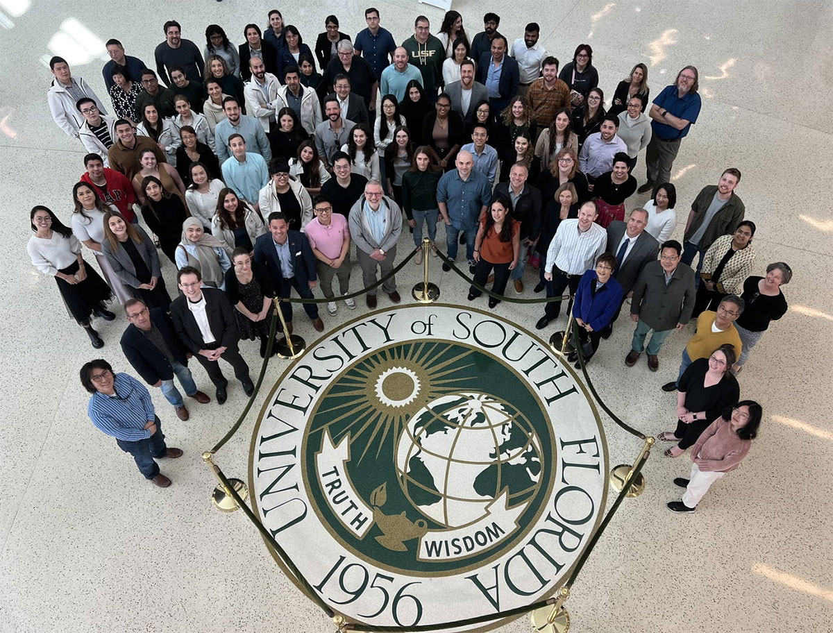 Downward shot of USF Health MPP staff and faculty standing around USF crest on the floor