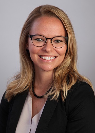Rachael Griffin smiling wearing a beige blouse with a black blazer and black beaded necklace and black framed glasses