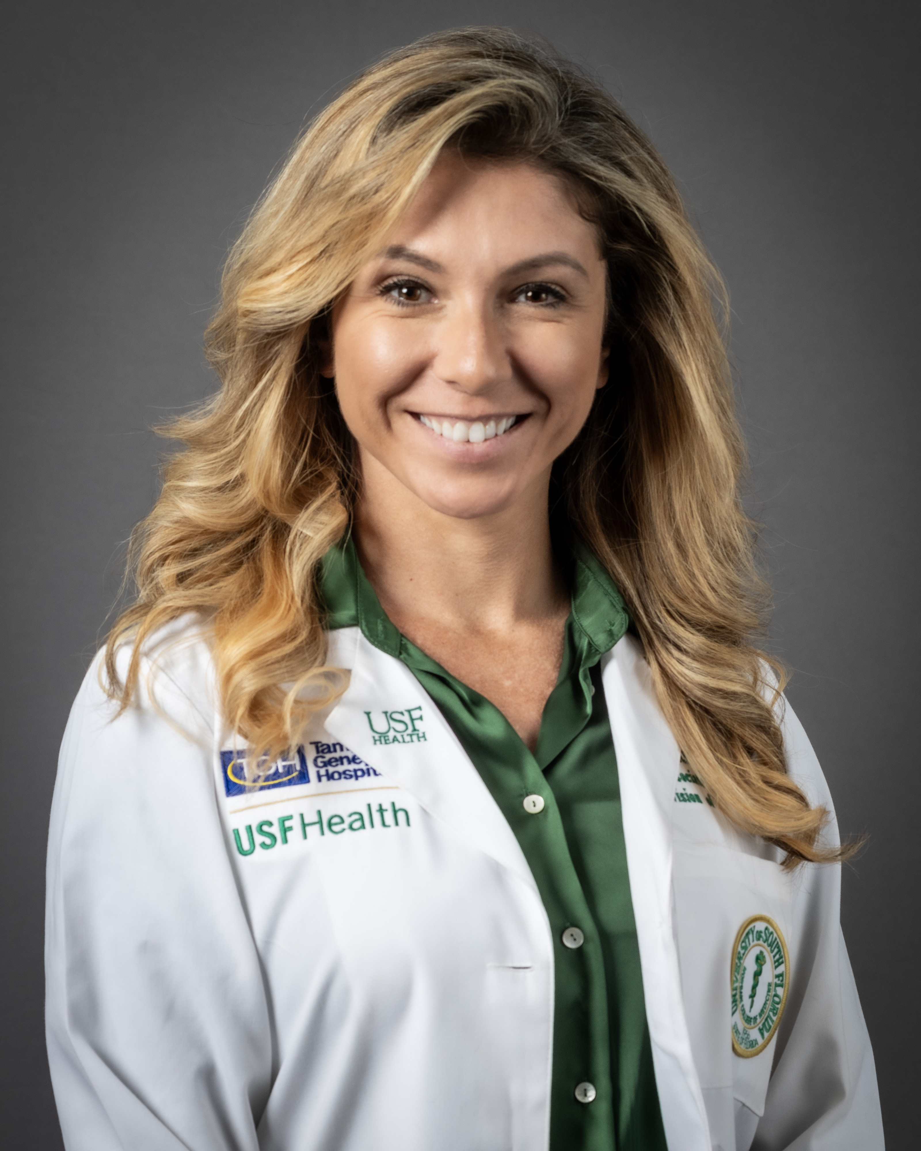 Headshot of Dr. Dimou in a white coat and green button up top.