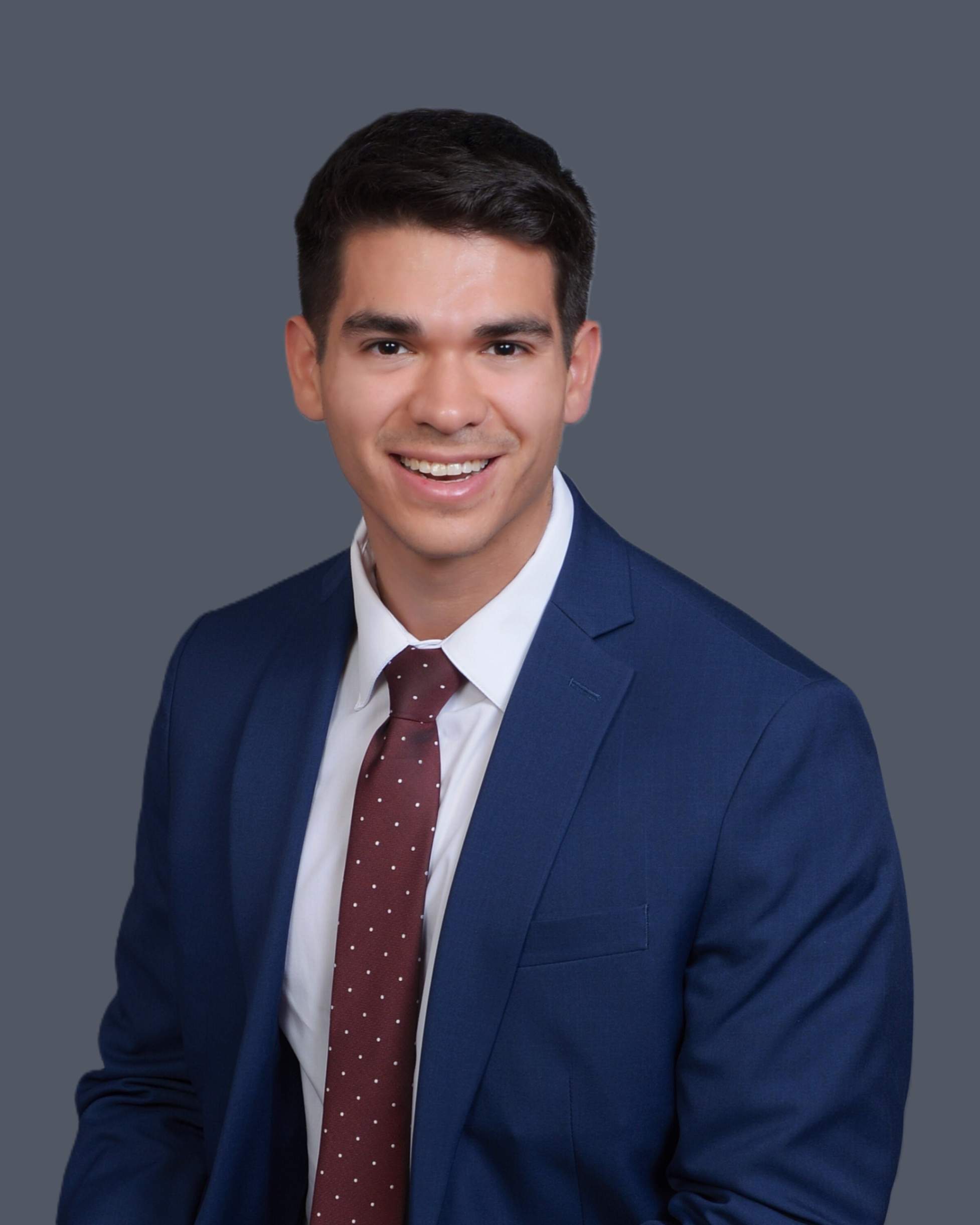 A headshot of Dr. Malavet in a blue suit, white button down, and red tie