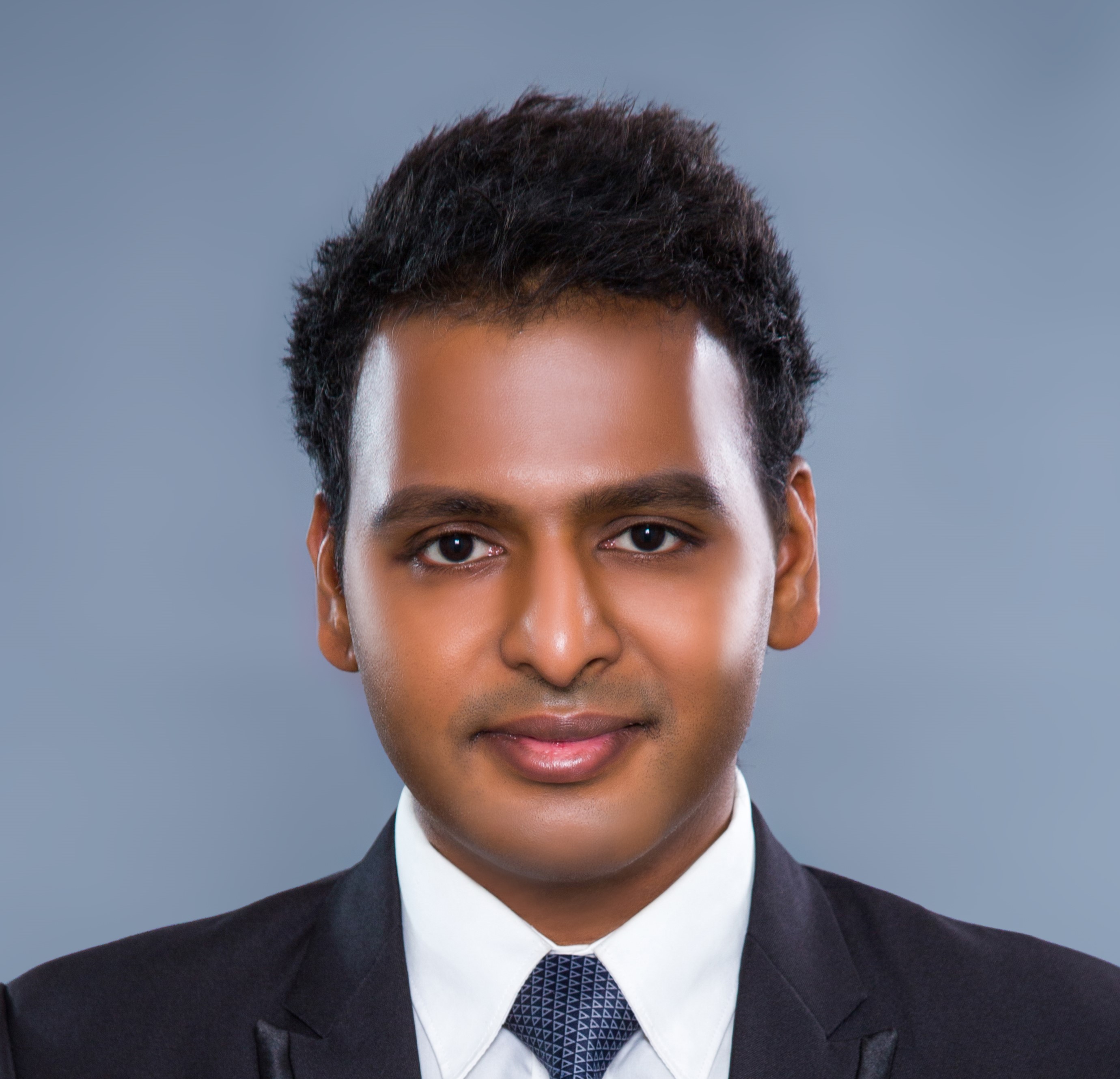 Ojas Natarajan smiling wearing a suit and tie with a blue background