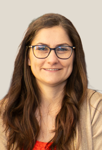 Marta Toth smiling wearing black glasses, a tan sweater and red shirt