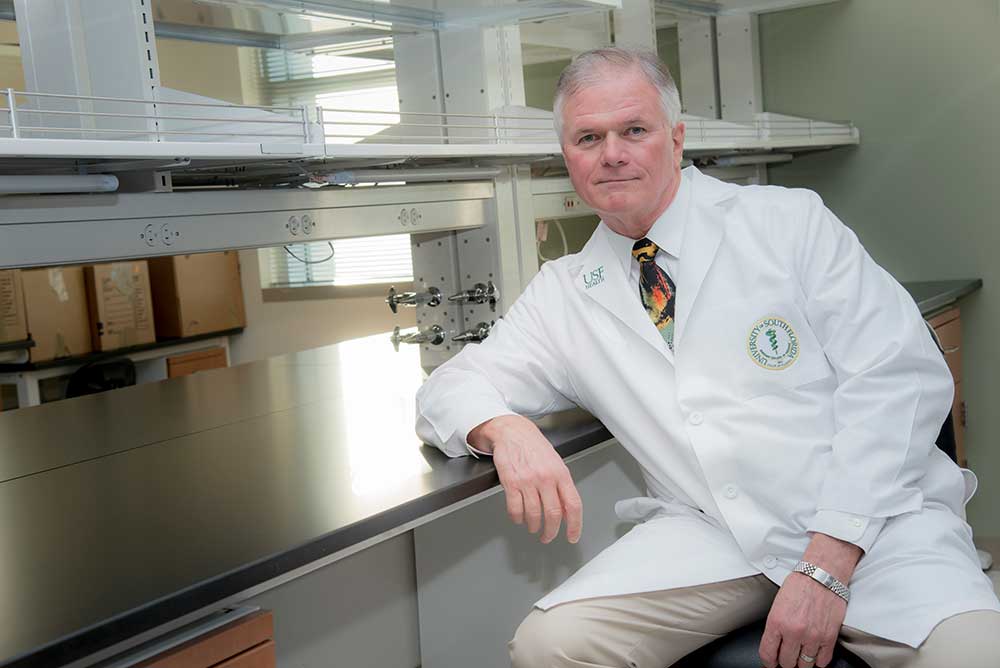 Dr Wickline seated in front of laboratory table with safety hoods
