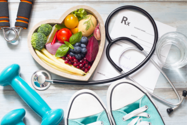 Various items depicting lifestyle medicine, including a heart-shaped bowl of fruits and vegetables, weights, sneakers, and a stethoscope.