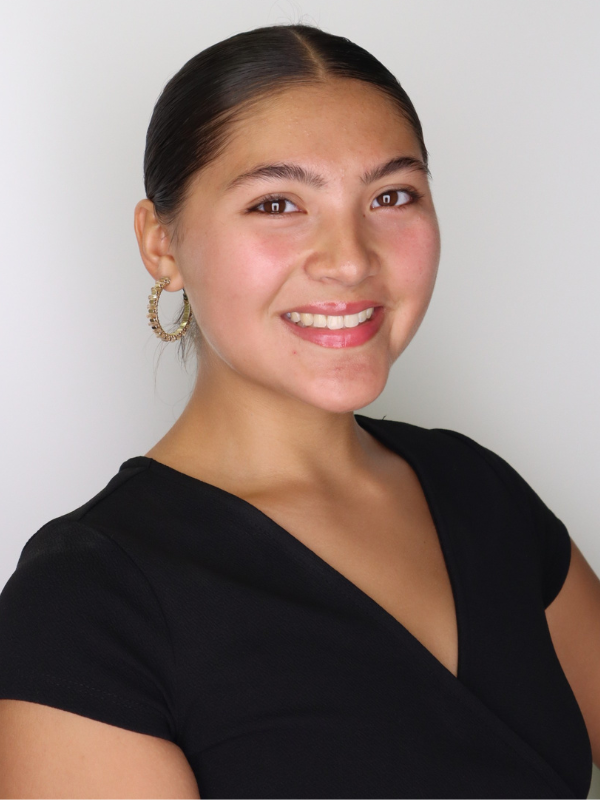 A headshot of Madisen Phonathong in front of a white backdrop. She is smiling and wearing a black top.