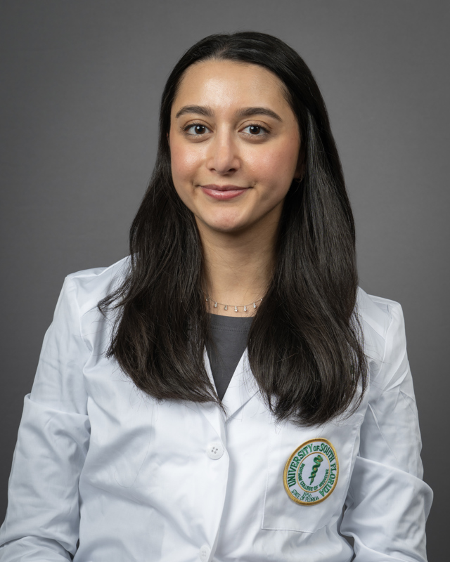 Rama Abdin smiling wearing a grey blouse and a USF Health branded medical white coat